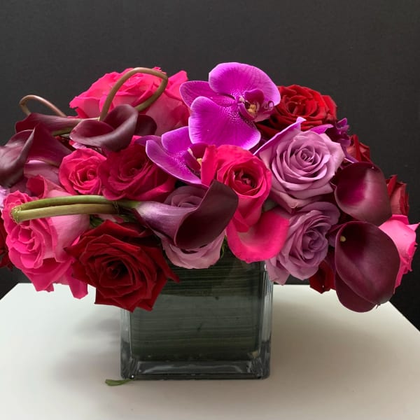 Bouquet of pink and red roses with purple orchids in a square glass vase