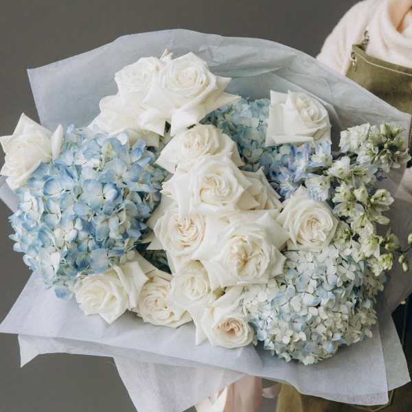Bouquet of white roses and pale blue hydrangeas wrapped in paper