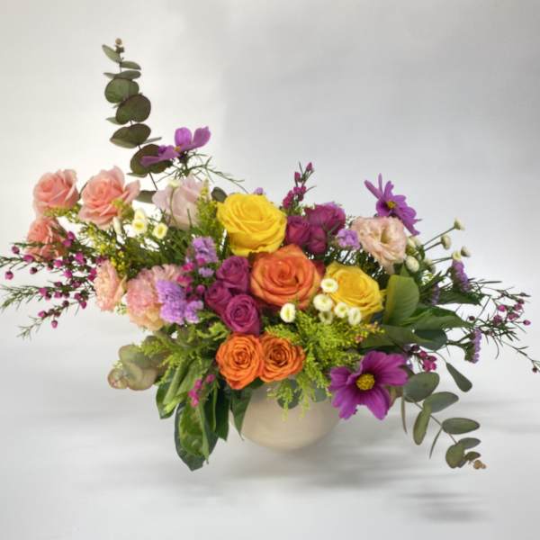 Mixed bouquet of roses and purple daisies in a round vase
