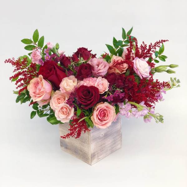 Pink and burgundy roses arranged in a wooden box