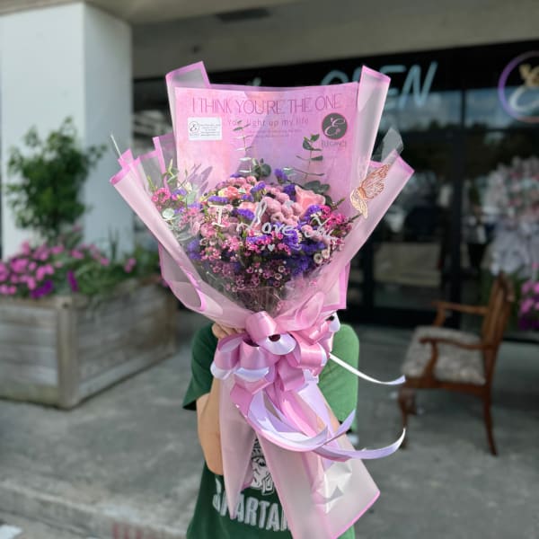 Pink and purple bouquet wrapped in pink paper with a ribbon bow