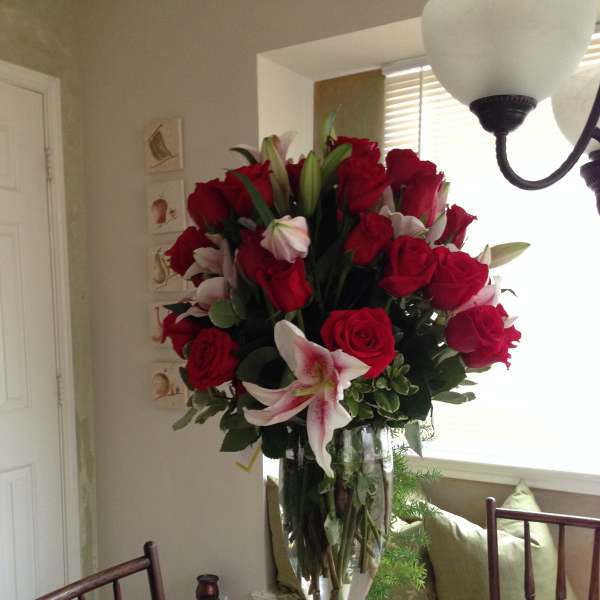 Tall bouquet of red roses and pink lilies in a clear glass vase