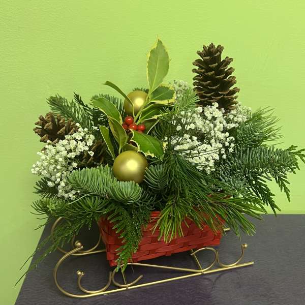 Holiday arrangement in a red basket with pinecones, white filler flowers, and gold ornaments
