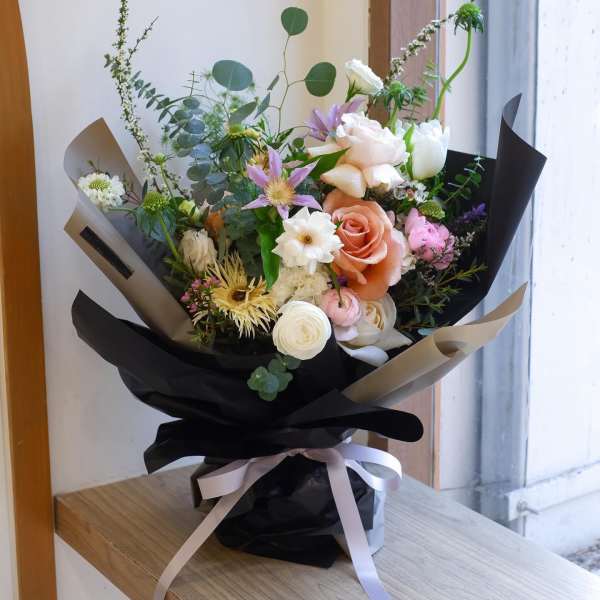 Mixed bouquet of pastel flowers wrapped in black paper with a ribbon