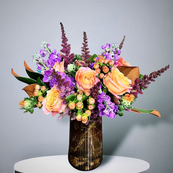 Bouquet of peach roses and purple flowers in a ribbed glass vase