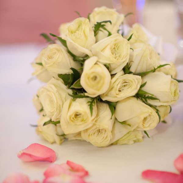 Bouquet of cream roses with pink petals scattered nearby