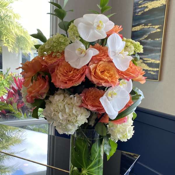 Orange roses and white orchids arranged in a tall glass vase