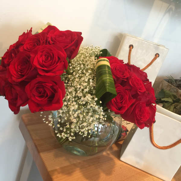 Red roses arranged in a glass vase with baby's breath and leaf wraps