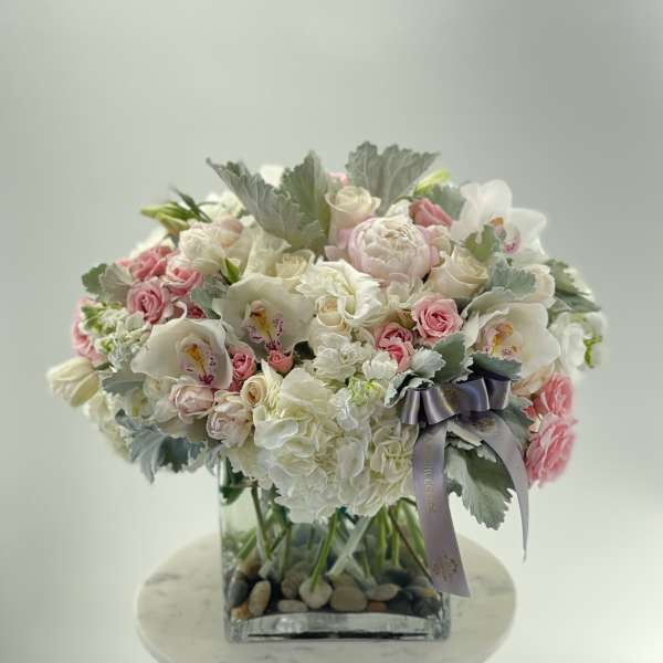 Pink and white floral arrangement in a square glass vase with a ribbon