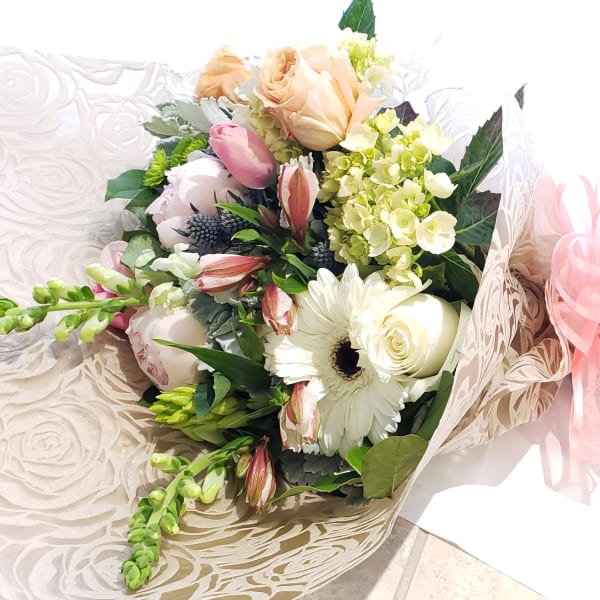 Bouquet of white and blush flowers wrapped in patterned paper with a pink ribbon