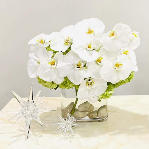 White orchid arrangement in a clear rectangular vase with decorative stones