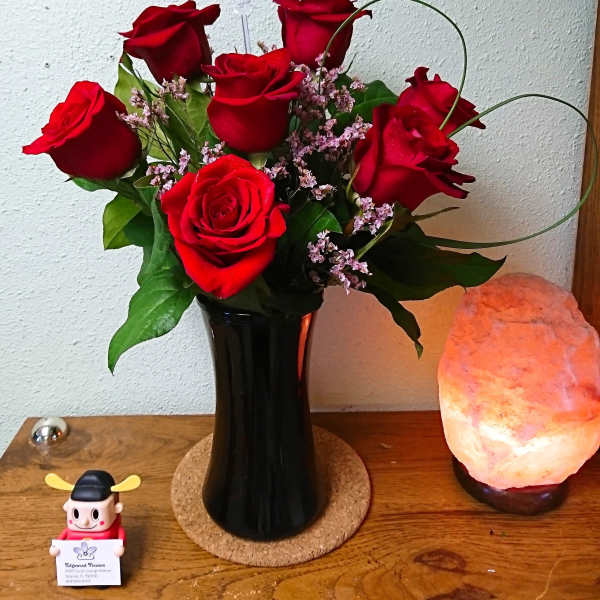 Red roses arranged in a black vase with small pink filler flowers