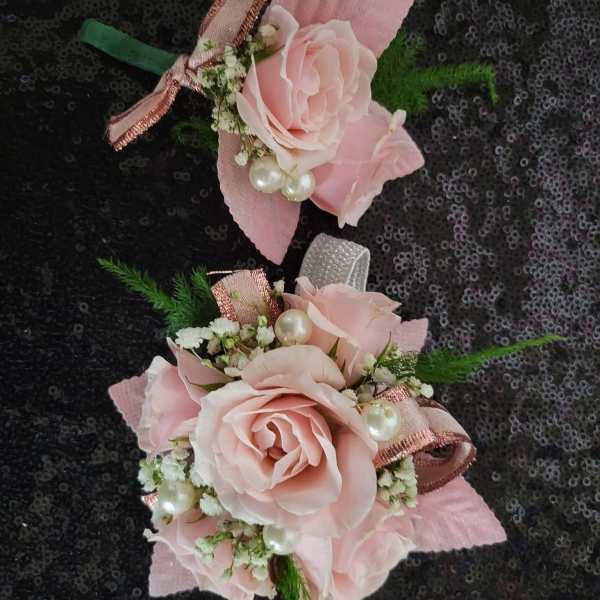 Two pink rose corsages with ribbon and pearl accents on a dark sequined background