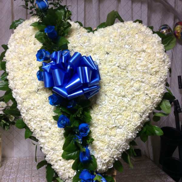 Heart-shaped white floral arrangement with blue roses and a blue ribbon