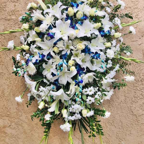 Large white floral spray with lilies and orchids on a tan wall