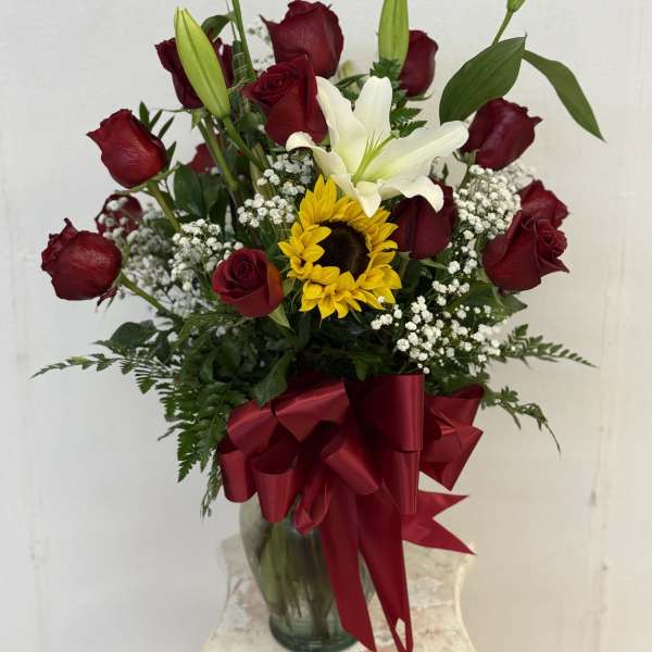 Bouquet of red roses, a white lily, and a sunflower in a glass vase