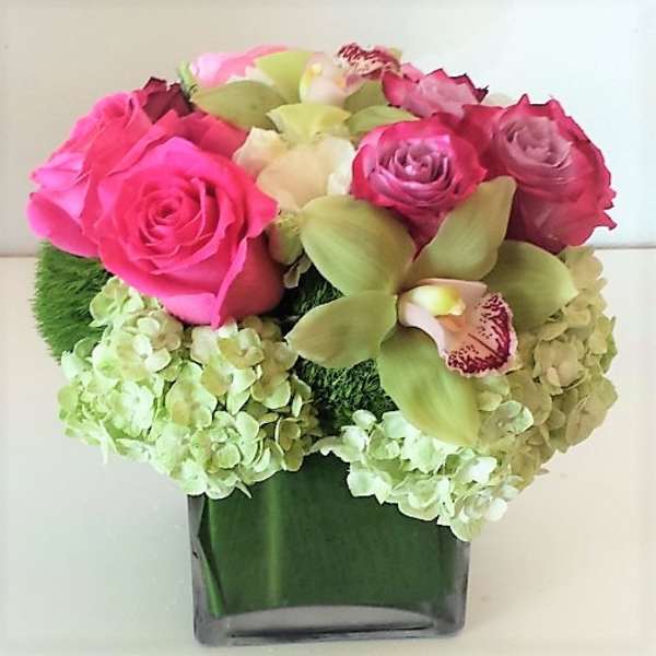 Pink roses and green orchids arranged in a square glass vase