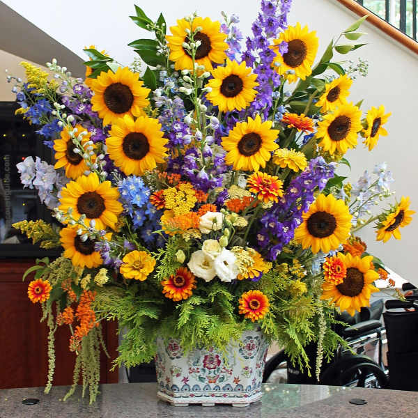 Large mixed bouquet with sunflowers, purple spikes, and a patterned ceramic vase