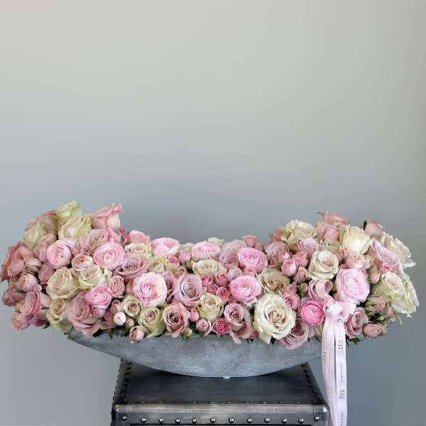 Low arrangement of pink and cream roses in a gray container