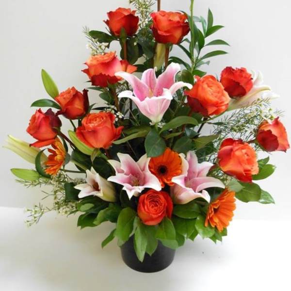 Tall arrangement of orange roses, pink lilies, and orange gerbera daisies in a black vase
