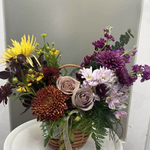 Basket arrangement of mixed flowers in yellow, purple, pink, and burgundy