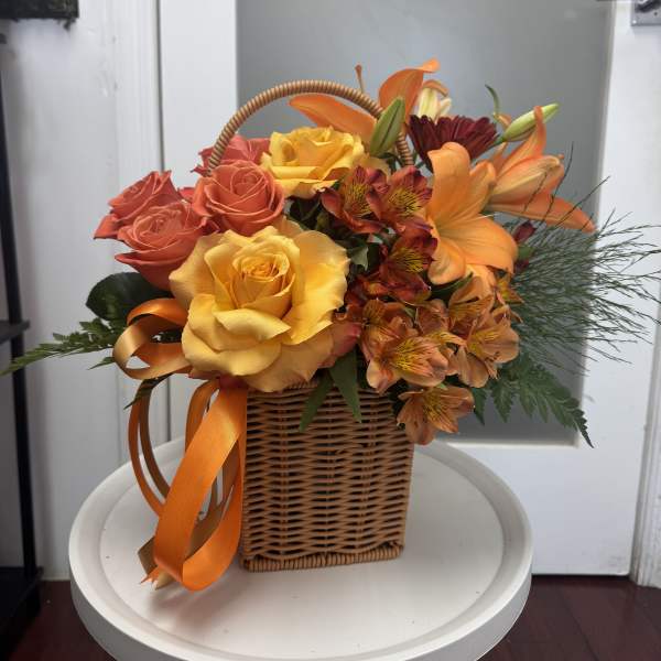 Basket of orange and yellow roses with lilies and ribbon
