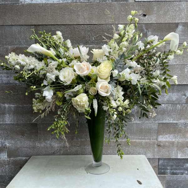 White floral arrangement in a tall green vase with cascading stems
