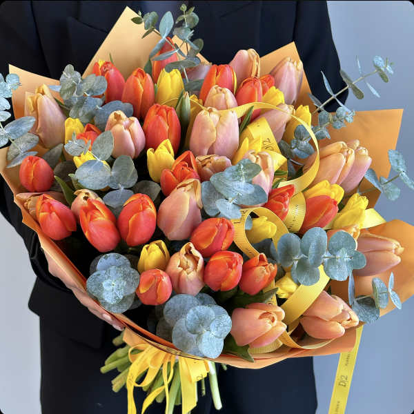 Handheld bouquet of multicolored tulips with blue eucalyptus accents