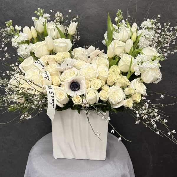 White floral arrangement in a tall square vase with roses and tulips