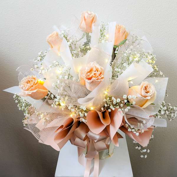 Peach roses with baby's breath and ribbon in a wrapped bouquet