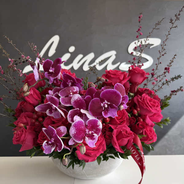 Pink roses and purple orchids arranged in a round glass bowl