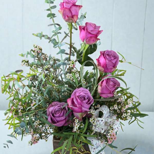 Purple roses in a wooden box with airy greenery and small white filler flowers