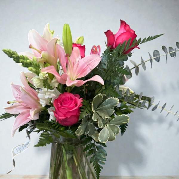 Pink lilies and roses arranged in a clear glass vase