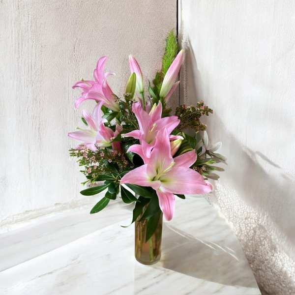 Pink lilies arranged in a clear glass vase with greenery