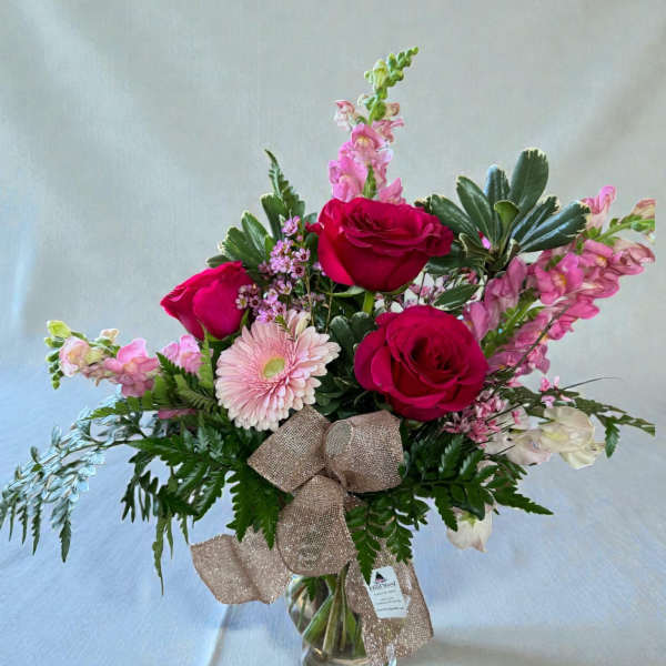 Bouquet of red roses and pink flowers in a glass vase with a ribbon