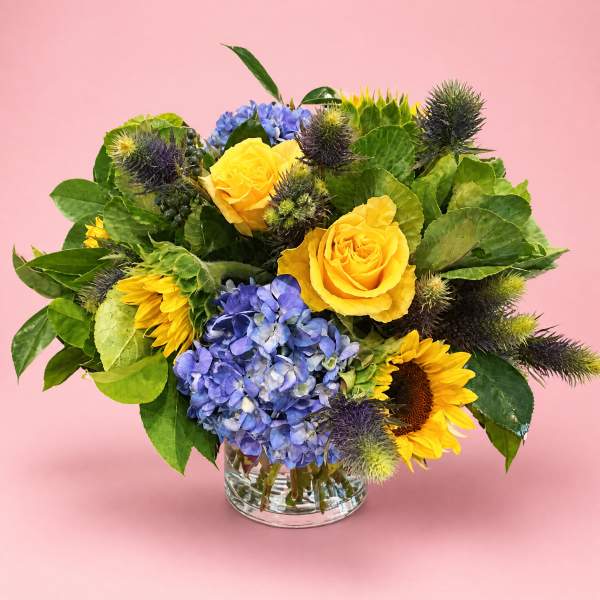 Yellow roses and blue hydrangeas in a clear glass vase