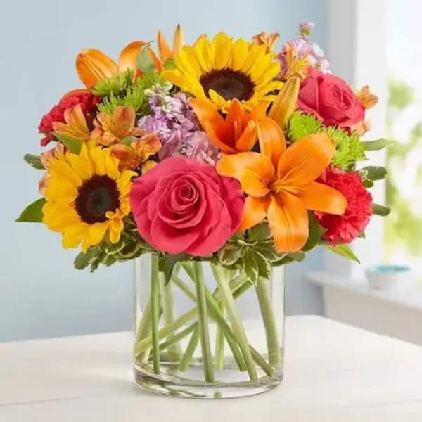Mixed bouquet of sunflowers, roses, and lilies in a clear glass vase