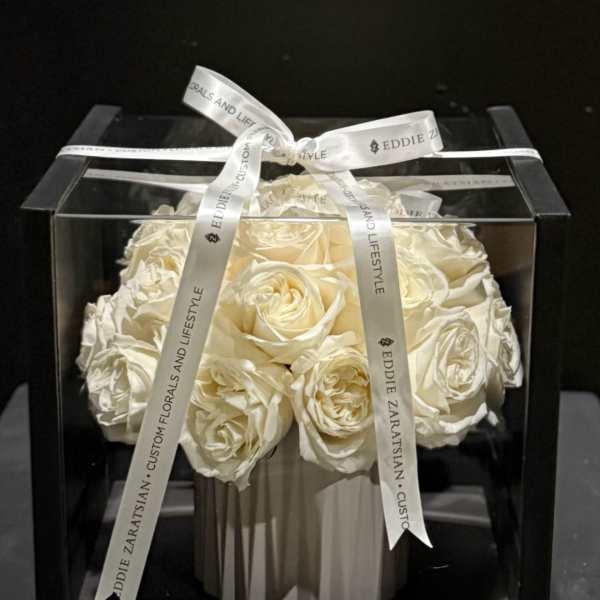 White roses arranged in a black gift box with a ribbon bow