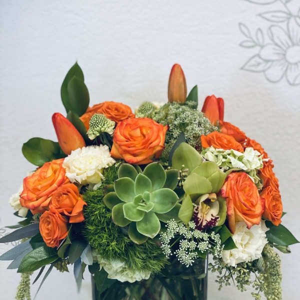 Orange roses and succulents arranged in a square glass vase