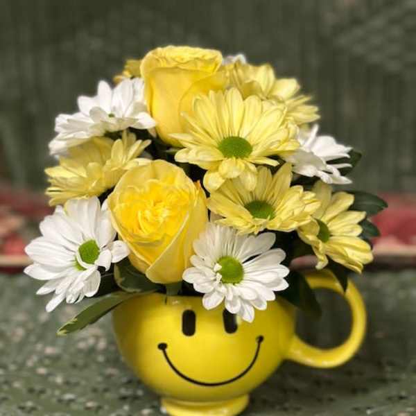 Yellow and white flowers arranged in a smiley-face mug