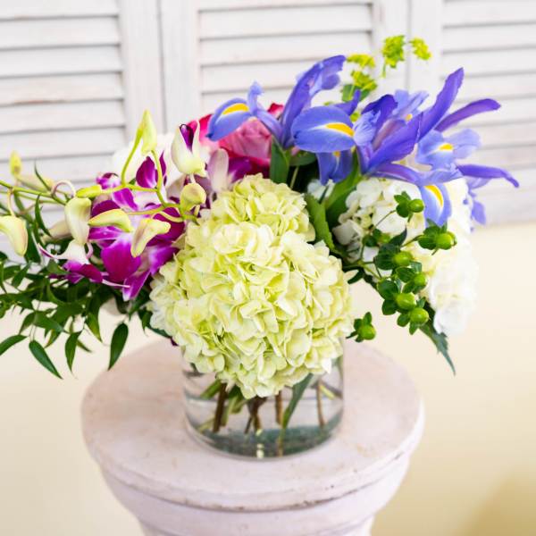 Colorful bouquet with blue irises, white hydrangea, and purple orchids in a glass vase