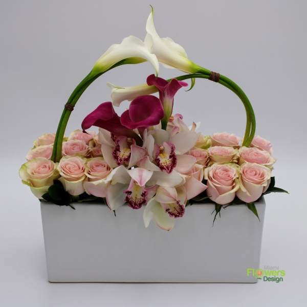 Pink roses and white calla lilies arranged in a white box with an arched handle