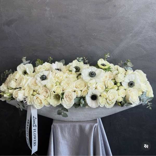 Long white floral arrangement with roses and anemones in a low container