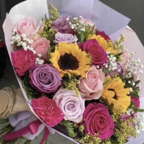 Bouquet of pink and purple roses with sunflowers in pastel wrapping