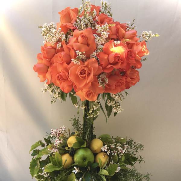 Orange roses in a tall vase with lemons and greenery