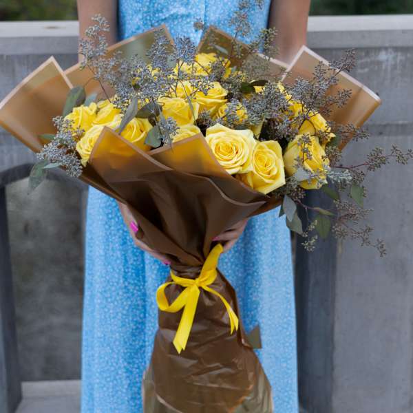 Bouquet of yellow roses wrapped in brown paper with a yellow ribbon