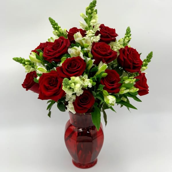 Red roses and white snapdragons arranged in a red glass vase.