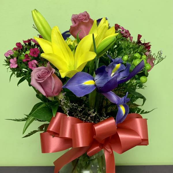 Bouquet of yellow lilies, purple irises, and pink roses in a glass vase with a red ribbon