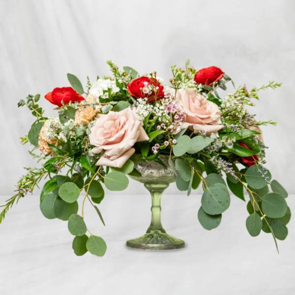 Low floral arrangement in a green glass pedestal vase with pink and red roses