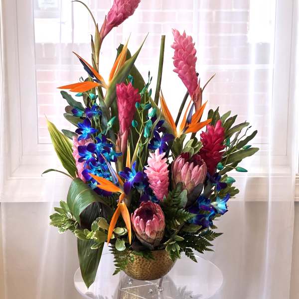 Tropical arrangement with pink ginger, bird of paradise, and orchids in a gold vase